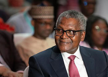 Senior professional man wearing glasses at formal event, listening attentively with diverse audience in background.