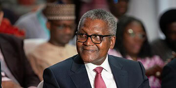 Senior professional man wearing glasses at formal event, listening attentively with diverse audience in background.