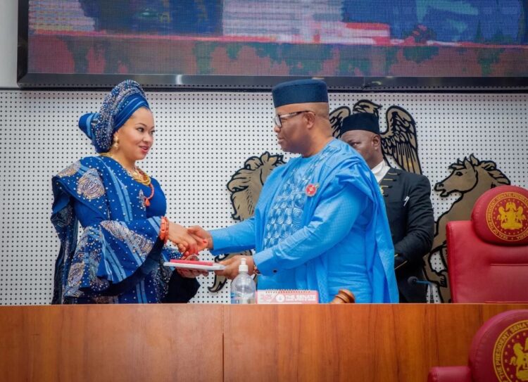 Elegant Nigerian woman in traditional blue attire shaking hands with official in blue traditional robe during formal event at the senate chamber.
