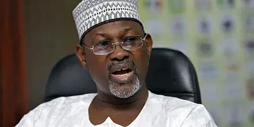 Elderly man wearing traditional attire and glasses, sitting in an office setting, speaking passionately during a discussion or interview.