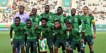 Midfielder holding Nigeria national football team flag, wearing green kit during match, with teammates on football field, fans in stadium background, active sports scene, Nigeria football team, African football competition.