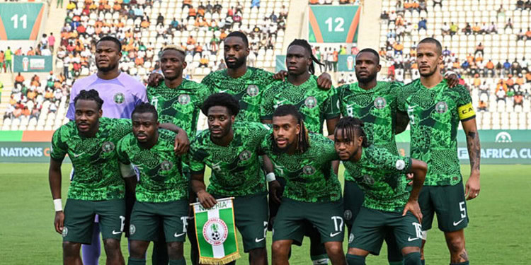 Midfielder holding Nigeria national football team flag, wearing green kit during match, with teammates on football field, fans in stadium background, active sports scene, Nigeria football team, African football competition.