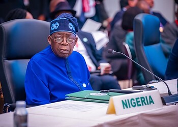 Nigerian delegate at international conference, wearing traditional blue outfit and sitting at a desk with Nigeria country label, engaged in global policy discussions about freelanews and freelance economy.