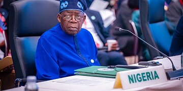 Nigerian delegate at international conference, wearing traditional blue outfit and sitting at a desk with Nigeria country label, engaged in global policy discussions about freelanews and freelance economy.
