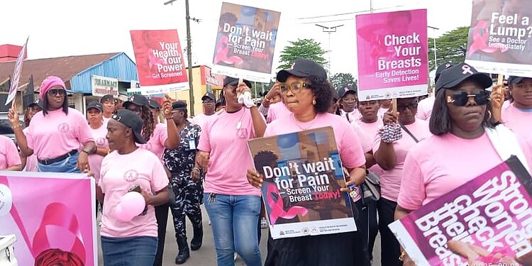 Breast cancer awareness march with women holding signs promoting early detection and health checkups, wearing pink outfits on a street.