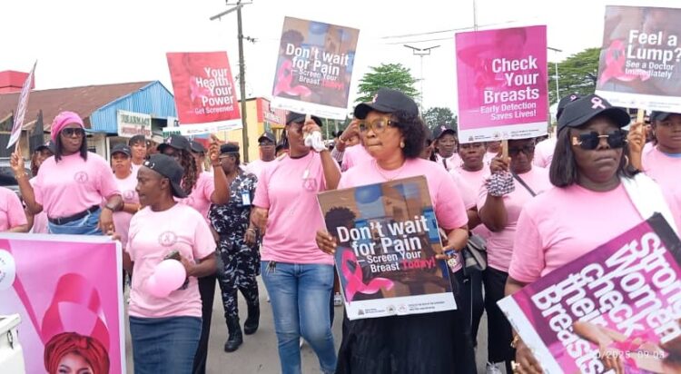 Breast cancer awareness march with women holding signs promoting early detection and health checkups, wearing pink outfits on a street.