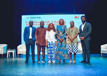 Diverse group of professionals at a conference or seminar on stage with a large screen displaying "Calling All TATA Women Entrepreneurs" in the background, showcasing women empowerment and entrepreneurship.