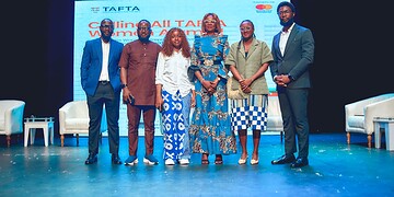 Diverse group of professionals at a conference or seminar on stage with a large screen displaying "Calling All TATA Women Entrepreneurs" in the background, showcasing women empowerment and entrepreneurship.