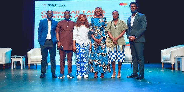 Diverse group of professionals at a conference or seminar on stage with a large screen displaying "Calling All TATA Women Entrepreneurs" in the background, showcasing women empowerment and entrepreneurship.