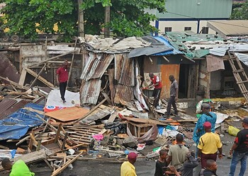 Collapsed makeshift housing in an informal settlement with people assessing the damage and working amidst the debris and wreckage.
