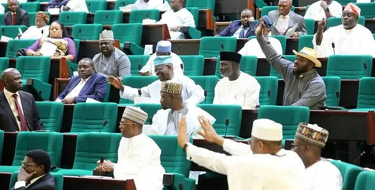 Seated lawmakers and officials engaged in a parliamentary debate in a legislative chamber with green seats.