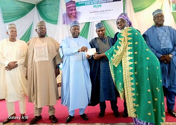 Award ceremony in Nigeria, with traditional attire and Nigerian flag in background, celebrating achievements with dignitaries and community leaders.