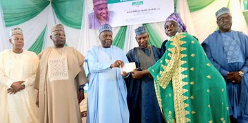 Award ceremony in Nigeria, with traditional attire and Nigerian flag in background, celebrating achievements with dignitaries and community leaders.