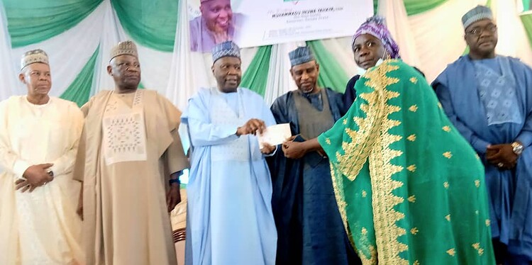 Award ceremony in Nigeria, with traditional attire and Nigerian flag in background, celebrating achievements with dignitaries and community leaders.