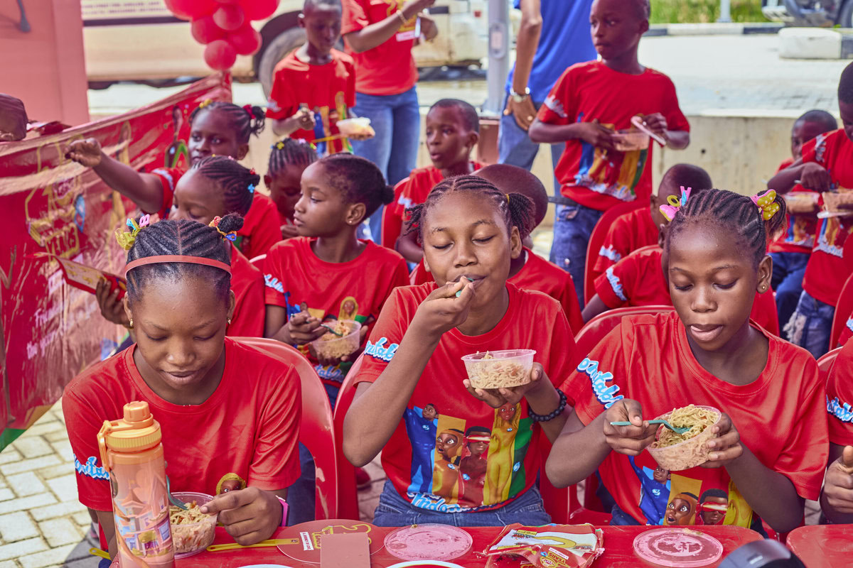 Children enjoying a celebratory event with red themed decorations and food, wearing matching red shirts, in an outdoor setting.