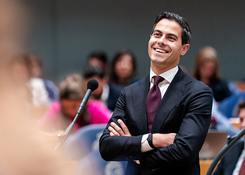 Business professional smiling at a conference or seminar, representing leadership and corporate success, with a diverse audience in the background.