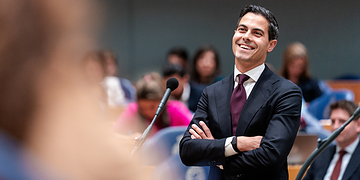 Business professional smiling at a conference or seminar, representing leadership and corporate success, with a diverse audience in the background.