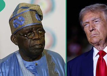 Elderly African man wearing traditional blue attire and glasses alongside a portrait of Donald Trump in a dark setting.