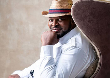 Stylish man wearing a straw hat and white shirt, sitting confidently on a modern chair, representing freelancing, creativity, and confidence in the workplace.