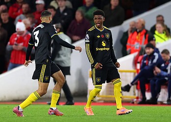 Dynamic football players celebrating a goal during a match, wearing black and yellow team kits, on a well-lit stadium with enthusiastic spectators in the background.