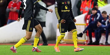 Dynamic football players celebrating a goal during a match, wearing black and yellow team kits, on a well-lit stadium with enthusiastic spectators in the background.