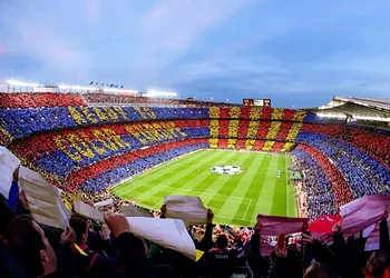 Fans holding colourful banners and scarves in a packed football stadium during a live UEFA Champions League match.