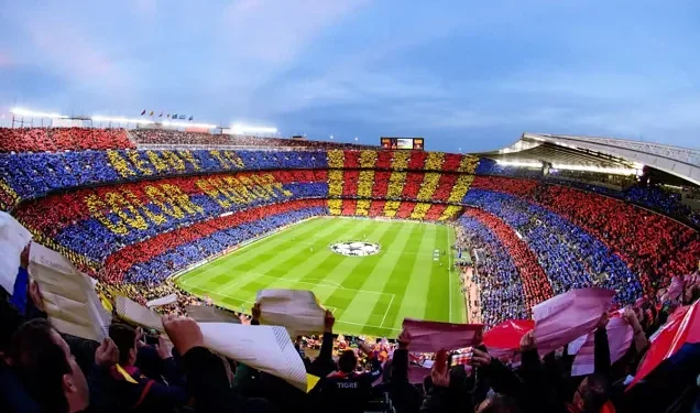 Fans holding colourful banners and scarves in a packed football stadium during a live UEFA Champions League match.