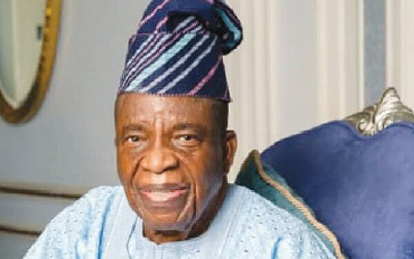 Elderly man wearing traditional Yoruba cap sitting on a luxurious sofa, showcasing cultural fashion and elegance.