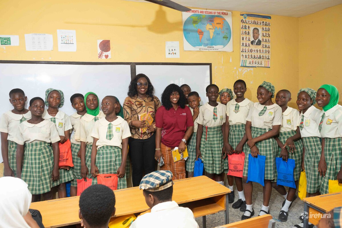 Girls in school uniform with two women standing in classroom in front of world map and educational posters.