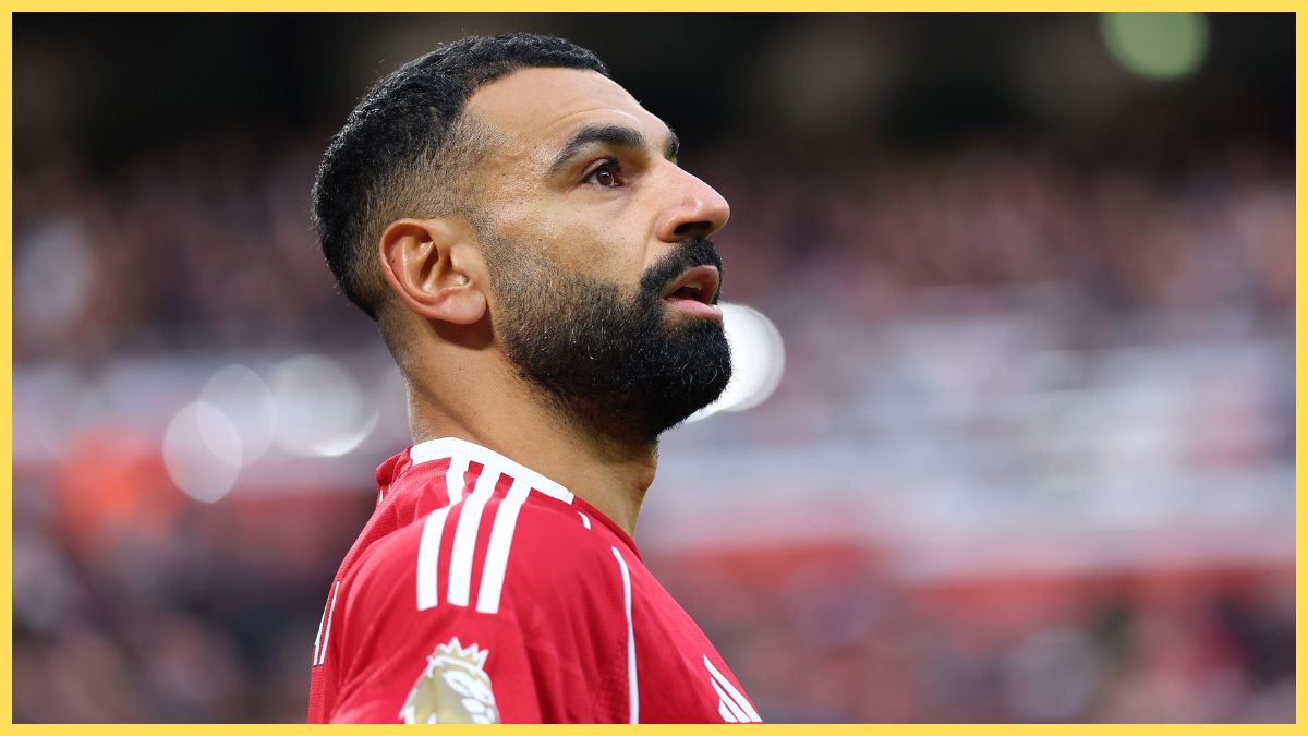 An athlete with a beard and short dark hair, wearing a red sports jersey, on a football pitch during a match, representing popular sports news and football updates.
