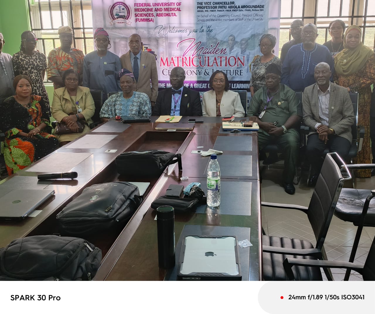 1. Group photo of university officials and attendees at a matriculation ceremony in a conference room with a banner in the background.