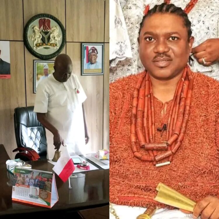 A government official in a white outfit standing in an office with framed photos and emblems on the wall, representing official political or administrative context in Nigeria.