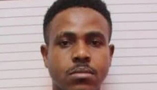 Young professional man with serious expression in casual attire, standing in front of a white wall, representing modern freelancing and remote work lifestyle, ideal for freelance news coverage.