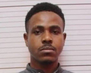 Young professional man with serious expression in casual attire, standing in front of a white wall, representing modern freelancing and remote work lifestyle, ideal for freelance news coverage.