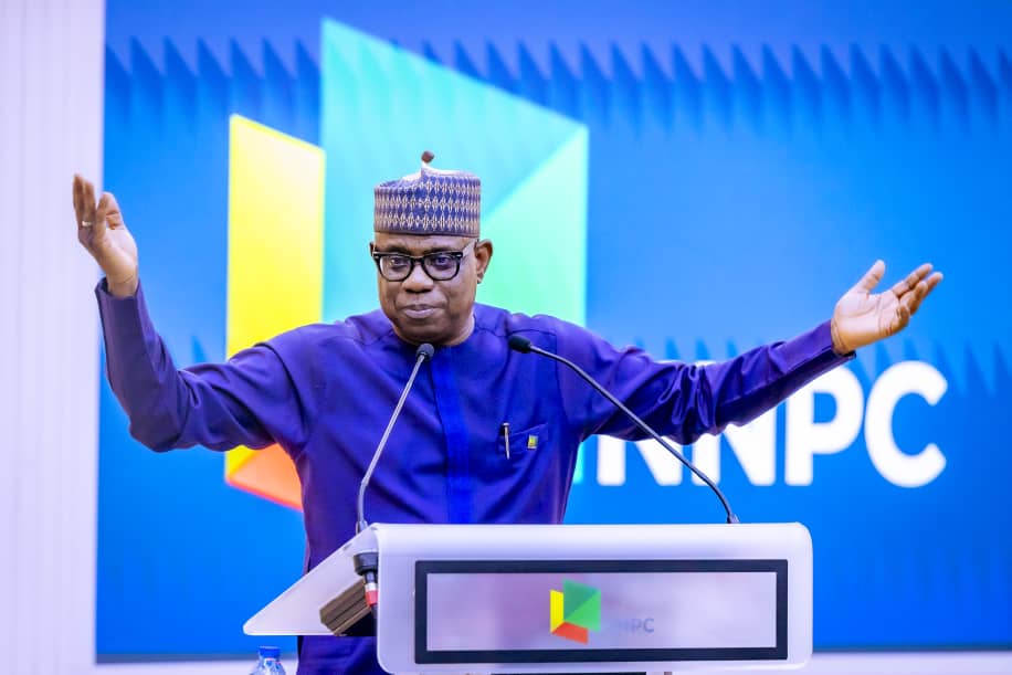 1. Nigerian politician in traditional attire speaking at a political event with KNPc logo in the background.