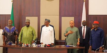 Senior Nigerian government officials during a formal meeting in the federal capital territory of Nigeria. The display includes photos of national leaders, national flags, and a gold emblem of Nigeria on the wall.