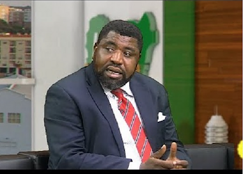 A professional man in a suit and striped tie speaking during a panel discussion or interview at Freelanews, with an urban backdrop and studio decor.