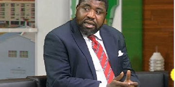 A professional man in a suit and striped tie speaking during a panel discussion or interview at Freelanews, with an urban backdrop and studio decor.