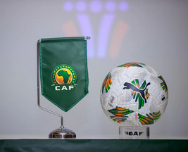 A close-up of the CAF flag and a colourful match ball on a table, symbolising African football tournaments and events. The image highlights sporting equipment associated with African Football Confederation activities.