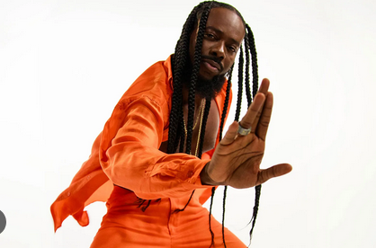 A stylish man with long braids in an orange outfit striking a confident pose, showcasing modern freelance lifestyle and creative energy for visual storytelling.