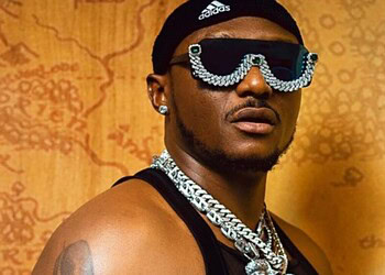 Vibrant portrait of a man wearing oversized sunglasses with jewel embellishments, layered chains, and stylish accessories, highlighting modern fashion and bold personal style.