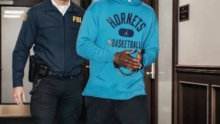 FBI agent arresting suspect wearing a blue 'Hornets Basketball' hoodie, in an indoor setting, highlighting law enforcement in action.