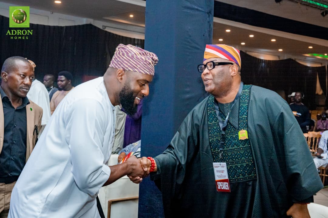 Handshake between two men at a professional event, wearing traditional attire, with other attendees in the background.