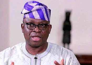 Vibrant close-up of a Nigerian man wearing traditional attire and glasses, speaking passionately, showcasing African culture, fashion, and leadership, in an indoor setting.