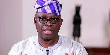 Vibrant close-up of a Nigerian man wearing traditional attire and glasses, speaking passionately, showcasing African culture, fashion, and leadership, in an indoor setting.