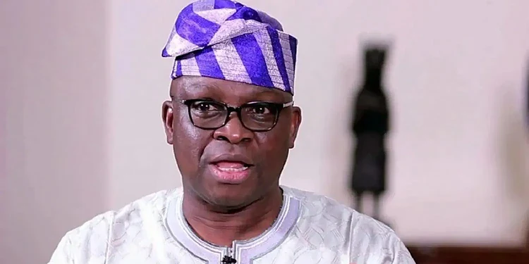 Vibrant close-up of a Nigerian man wearing traditional attire and glasses, speaking passionately, showcasing African culture, fashion, and leadership, in an indoor setting.
