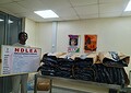 NDLDEA officer with seized drug packages and strategic command board, in a security or law enforcement environment.