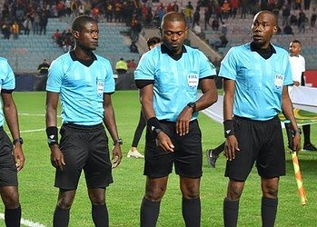 Referees in blue uniforms preparing for a football match in a stadium.