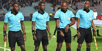 Referees in blue uniforms preparing for a football match in a stadium.