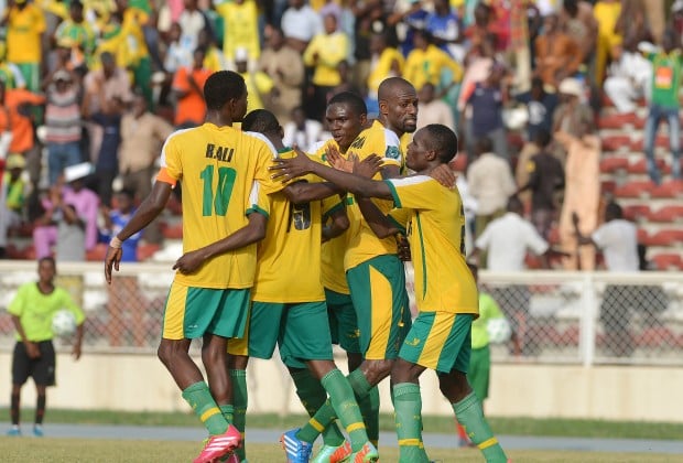 Excited Senegal football team celebrating a goal during a match in their vibrant yellow and green kit at the stadium. Fans cheering in the background, showcasing passion for African football.